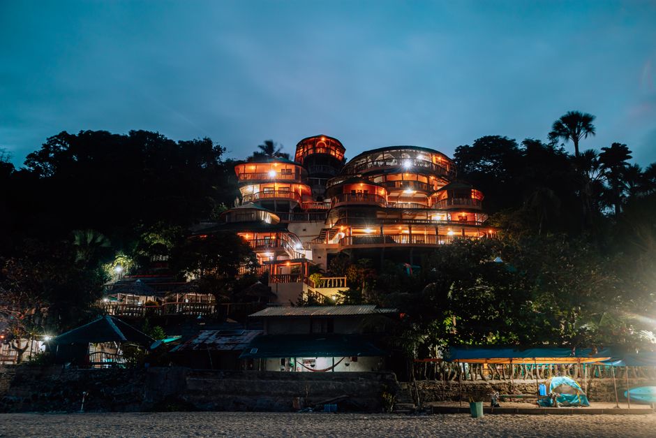 A beautifully illuminated beachfront resort with palm trees at twilight.