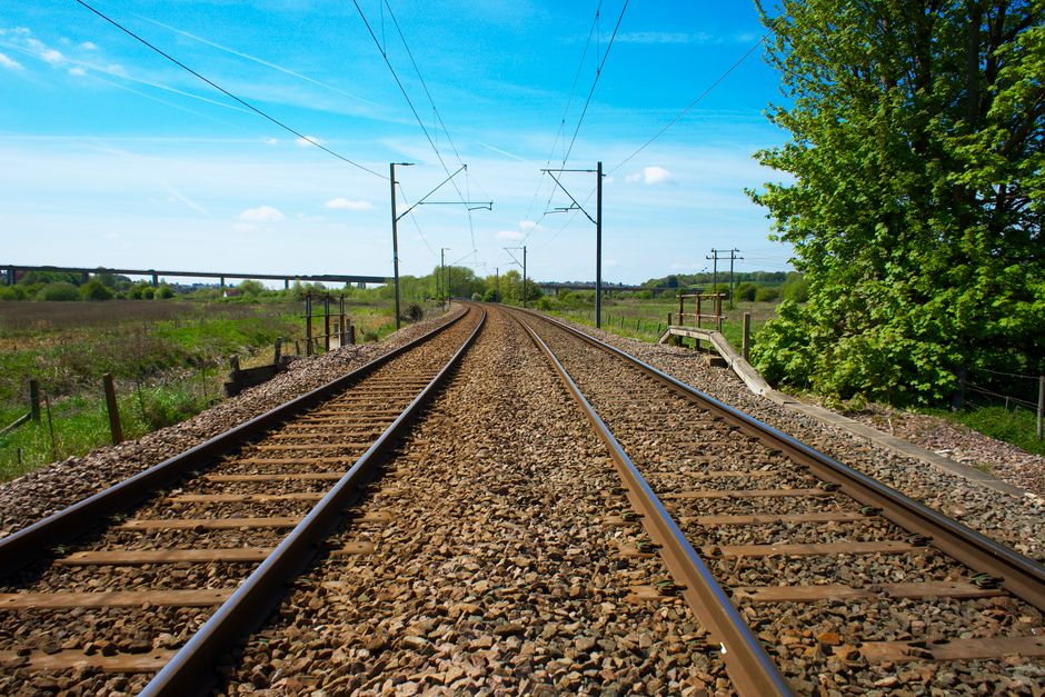 View of railway tracks stretching through the lush green UK countryside under a clear blue