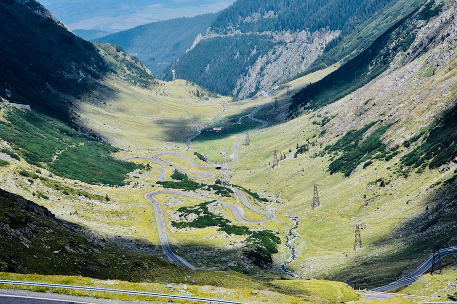 A winding road through lush valleys and rugged mountains in Buda, Romania. Perfect for nature lovers.